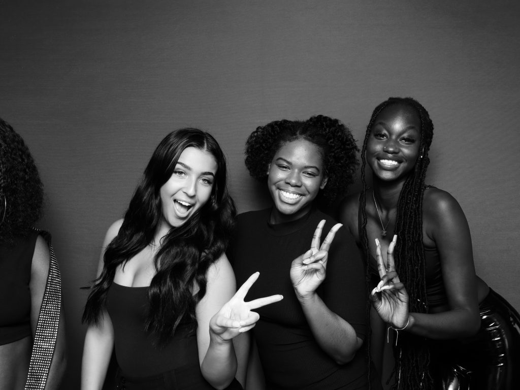 A black and white photo of a group of women posing at a glam photo booth.